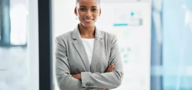 Liderança no setor público, sendo representada por uma mulher de braços cruzados, olhar confiante e sorrindo para a foto