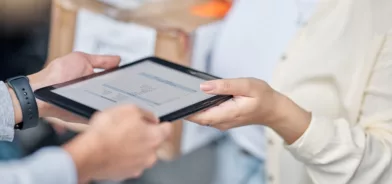 Pessoa entregando tablet à outra, em foto ilustrando importância da avaliação de fornecedores em contratações públicas