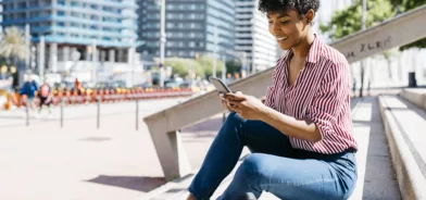 Mulher mexendo em celular enquanto está sentada em escada, em foto que ilustra post sobre governo como plataforma.