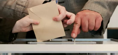 Pessoas colocando envelope em urna, em foto que ilustra post sobre lei de iniciativa popular. Foto: Arnaud Jaegers/Unsplash.