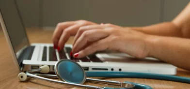 Médica usando computador, em foto que ilustra post sobre saúde municipal.