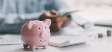 Mesa com cofrinho, calculadora e moedas, em foto que ilustra post sobre Fundo de Participação dos Estados. Reprodução: paegagz/Envato.
