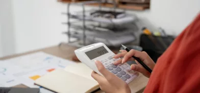 Mulher usando calculadora, ilustrando post sobre endividamento público. Foto: nateemee/Envato.