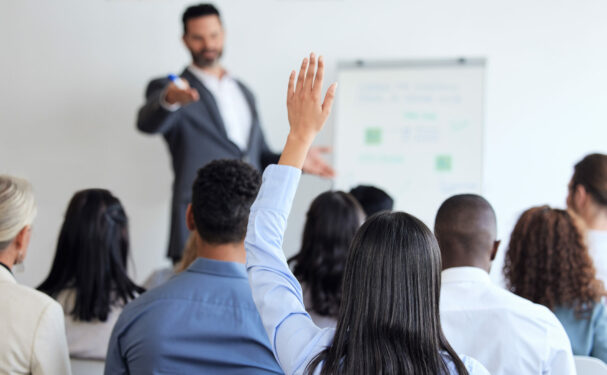 Pessoas em uma sala, uma levanta a mão, em foto que ilustra post sobre consulta pública. Foto: YuriArcursPeopleimages/Envato.