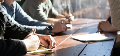 Pessoas assinando documentos e discutindo, em foto que ilustra post sobre participar de licitações. Foto: Dylan Gillis/Unsplash.