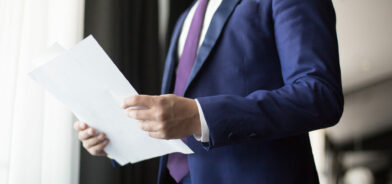Homem de terno segurando documentos, em foto que ilustra post sobre atos administrativos. Reprodução: Pressmaster/Envato.