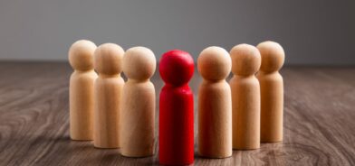 Figuras de madeira representando pessoas. No centro, há uma figura vermelha, destacando-se das demais figuras de cor natural. Foto que ilustra post sobre como ser um bom gestor. Foto: tehcheesiong/Envato.