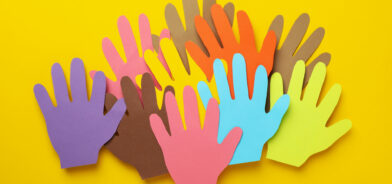 Silhuetas de mãos coloridas, recortadas em papel, sobre um fundo amarelo. As mãos são de diferentes cores, representando diversidade e colaboração e ilustrando um post sobre interesse público. Foto: AtlasComposer/Envato.
