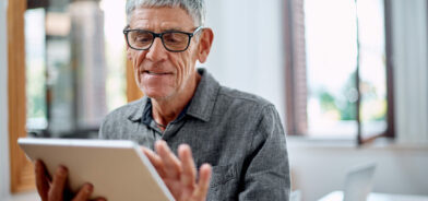 Homem idoso de cabelos grisalhos e óculos, segurando um tablet com uma expressão concentrada e leve sorriso. Foto que ilustra post sobre acessibilidade digital. Reprodução: YuriArcursPeopleimages/Envato.