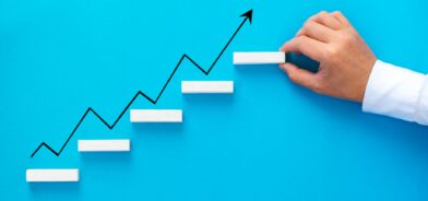 Mão de empresário organizando empilhamento de blocos de madeira como escada de degrau com seta de crescimento. Foto que ilustra escalabilidade. Reprodução: mihacreative/Envato.