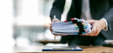 Homem com pilha de documentos impressos, em foto que ilustra post sobre organizações paperless. Reprodução: coolhand1180/Envato.