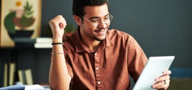 Jovem estudante sorridente durante estudo on-line olhando para a tela do tablet. Foto que ilustra post sobre educação digital. Reprodução: Pressmaster/Envato.