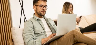 Homem usando computador, com mulher ao fundo usando celular. Foto que ilustra post sobre Marco Civil da Internet. Reprodução: BGStock72/Envato.