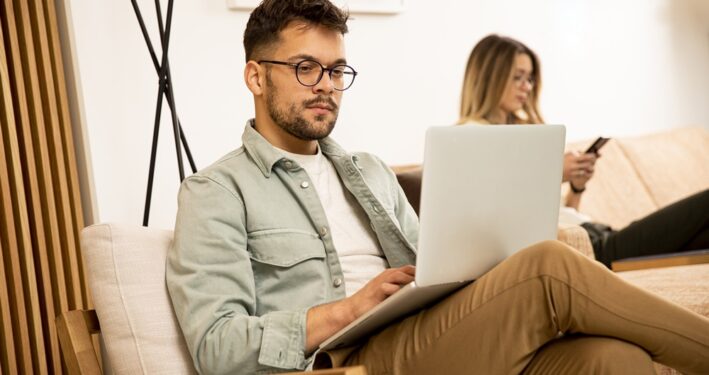 Homem usando computador, com mulher ao fundo usando celular. Foto que ilustra post sobre Marco Civil da Internet. Reprodução: BGStock72/Envato.