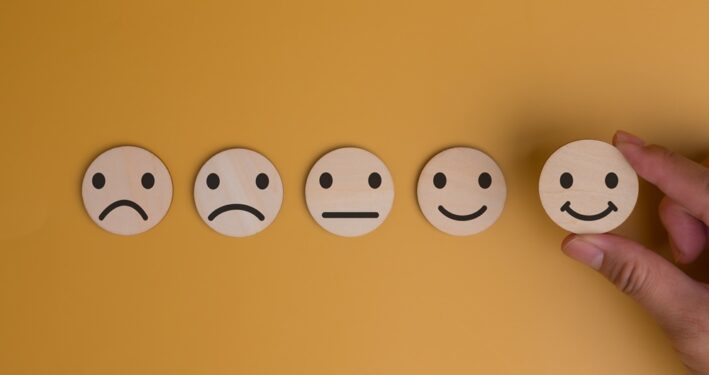 Uma mão escolhe um rosto sorridente entre uma sequência de expressões faciais, em foto que ilustra post sobre confiança institucional. Reprodução: donut3771/Envato.