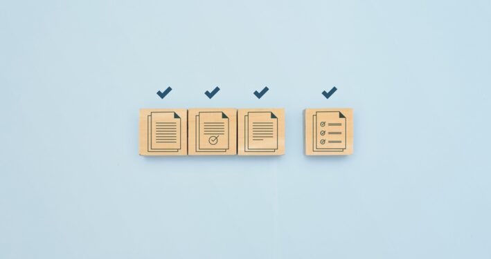 Uma ilustração minimalista que apresenta blocos de madeira com ícones de documentos e checkmarks, ilustrando post sobre compliance contratual. Reprodução: 1footage/Envato.