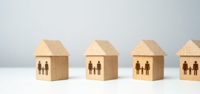 Casas de madeira com figuras de famílias pintadas em cada uma, simbolizando diversidade e inclusão no contexto habitacional, em post sobre programas sociais. Reprodução: iLixe48/Envato.