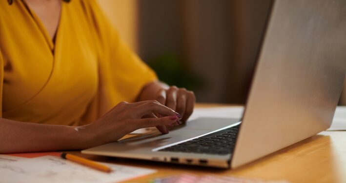 Mulher trabalhando em laptop, em foto que ilustra post sobre comunicados internos. Reprodução: DragonImages/Envato.