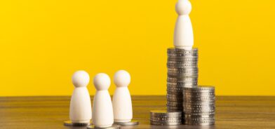 A imagem representa a desigualdade social, com três figuras sobre poucas moedas e uma figura isolada no topo de uma grande pilha de dinheiro, simbolizando a concentração de renda. Foto: tehcheesiong/Envato.