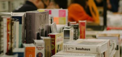 Uma fileira de livros em cima de uma mesa de madeira, em uma feira do livro. Foto que ilustra post sobre políticas culturais. Reprodução: Kate Bezzubets (@k8_bzz)/Unsplash.