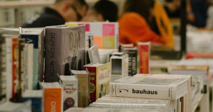 Uma fileira de livros em cima de uma mesa de madeira, em uma feira do livro. Foto que ilustra post sobre políticas culturais. Reprodução: Kate Bezzubets (@k8_bzz)/Unsplash.