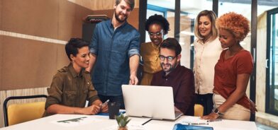 Foto de um grupo diversificado de empresários trabalhando juntos em um laptop em um escritório. Foto que ilustra post sobre economia criativa. Reprodução: YuriArcursPeopleimages/Envato.
