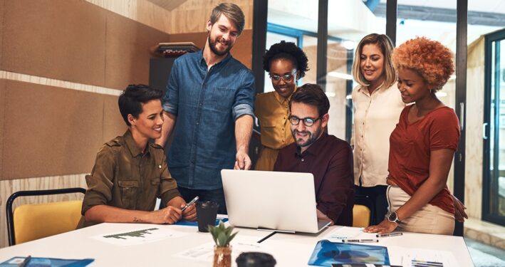 Foto de um grupo diversificado de empresários trabalhando juntos em um laptop em um escritório. Foto que ilustra post sobre economia criativa. Reprodução: YuriArcursPeopleimages/Envato.