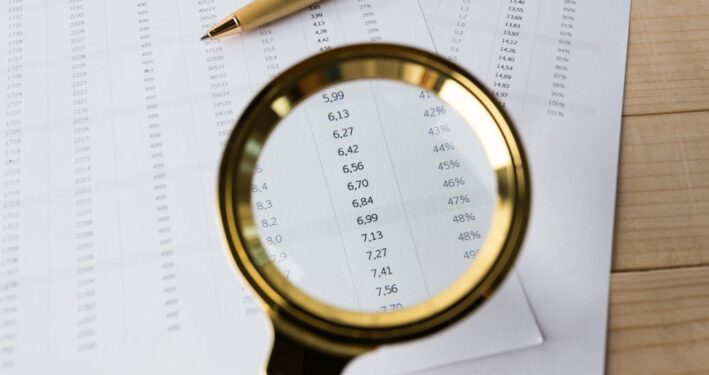 Lupa em relatório financeiro. Foto que ilustra post sobre Lei da Transparência Fiscal. Reprodução: FabrikaPhoto/Envato.