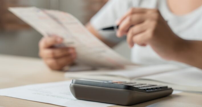 Mulher usando calculadora e anotações, em foto que ilustra post sobre taxa de expediente. Reprodução: stockerthings/Envato.