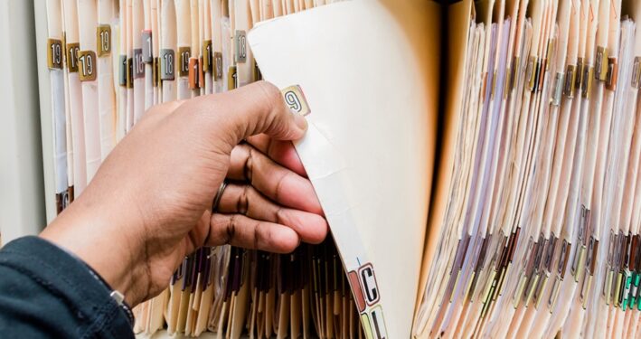 Pessoa manuseando documentos físicos, em foto que ilustra post sobre preservação de documentos. Reprodução: rohaneh/Envato.