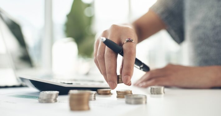 Pessoa contando moedas e fazendo conta em calculadora. Foto que ilustra post sobre dívida ativa municipal. Reprodução: YuriArcursPeopleimages/Envato.