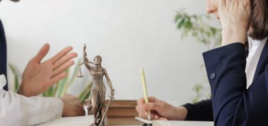 Duas pessoas analisando documentos ao lado de uma estátua da Justiça, em foto que ilustra post sobre sindicância. Reprodução: myjuly/Envato.