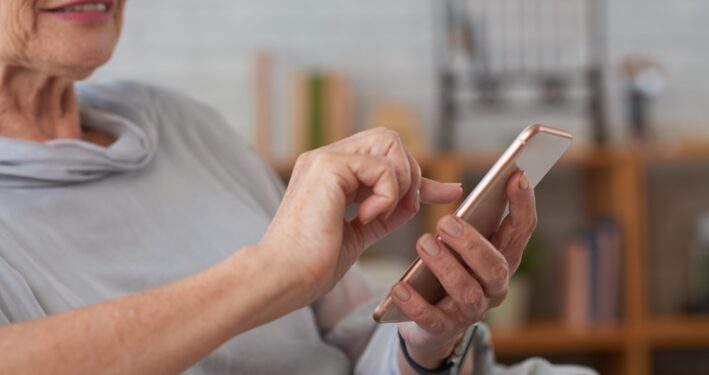 Mulher idosa usando smartphone, em foto que ilustra post sobre assistente virtual inteligente. Reprodução: DragonImages/Envato.