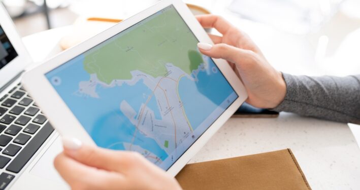 Mãos segurando tablet digital com mapa em exibição, em foto que ilustra post sobre planejamento urbano. Reprodução: Pressmaster/Envato.