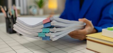 Pessoa segurando uma pilha de documentos. Em foto que ilustra post sobre projetos de Câmara sem papel. Reprodução: dekddui1405/Envato.
