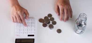 Pessoa contando moedas e fazendo contas em calculadora. Foto que ilustra post sobre Receita Corrente Líquida (RCL). Reprodução: wichayada69/Envato.