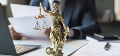 Advogado sentado à mesa, com estátua da justiça a frente dele. Foto que ilustra post sobre direito previdenciário. Reprodução: Pressmaster/Envato.