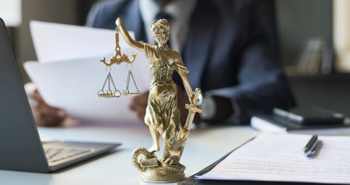 Advogado sentado à mesa, com estátua da justiça a frente dele. Foto que ilustra post sobre direito previdenciário. Reprodução: Pressmaster/Envato.