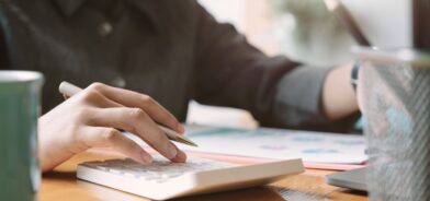 Mulher fazendo contas em calculadora, em foto que ilustra post sobre ciclo orçamentário. Reprodução: nateemee/Envato.