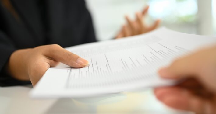 Pessoa entregando um documento para outra. Foto que ilustra post sobre falsificação de documento público. Reprodução: prathanchorruangsak/Envato.