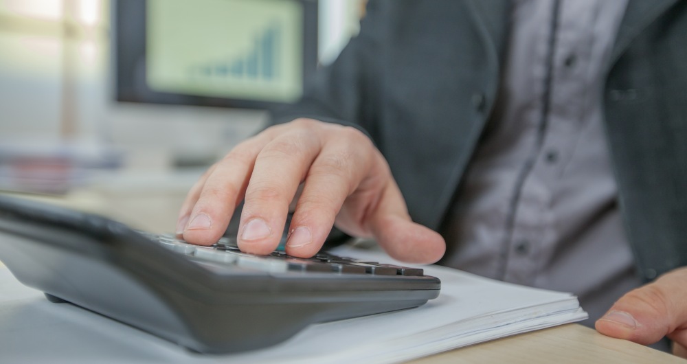 Homem fazendo contas em calculadora. Foto que ilustra post sobre duodécimo municipal. Reprodução: wirestock/Envato.