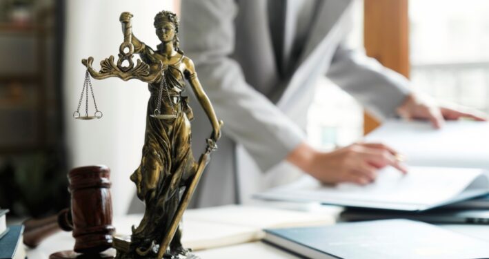 Pessoa avaliando leis, com estátua da justiça em primeiro plano. Foto que ilustra post sobre legislação orçamentária. Reprodução: ijeab/Envato.