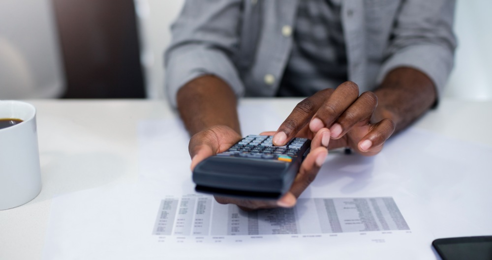 Homem fazendo contas em calculadora. Foto que ilustra post sobre balanço orçamentário. Reprodução: Wavebreakmedia/Envato.