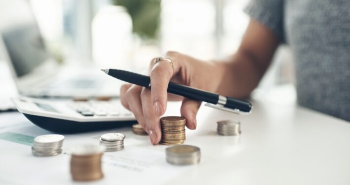 Foto aproximada de uma pessoa calculando finanças em um escritório. Ilustra post sobre caudas orçamentárias. Reprodução: YuriArcursPeopleimages/Envato.