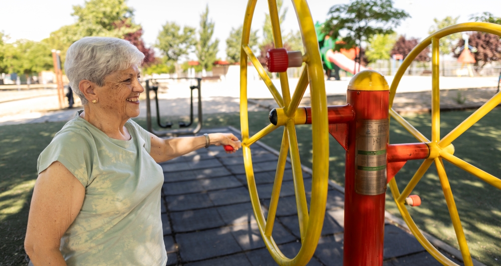 Idosa se exercitando em rodas de braço no parque ao ar livre. Foto que ilustra post sobre promoção da saúde. Reprodução: josecarloscerdeno/Envato.