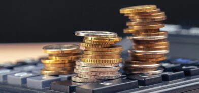 Moedas em cima de calculadora. Foto que ilustra post sobre retenção do IR. Reprodução: FabrikaPhoto/Envato.