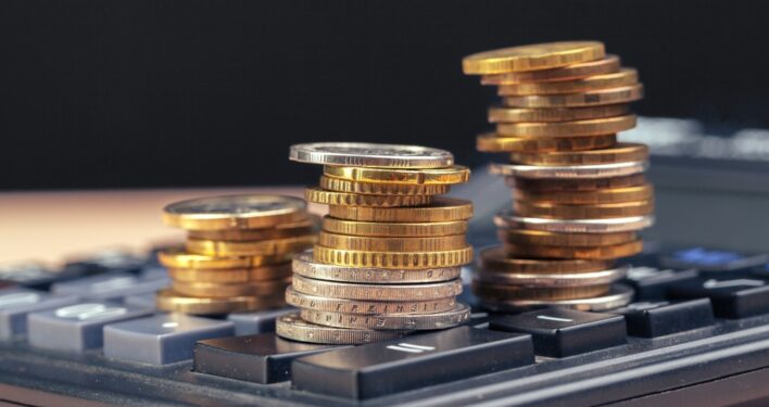 Moedas em cima de calculadora. Foto que ilustra post sobre retenção do IR. Reprodução: FabrikaPhoto/Envato.